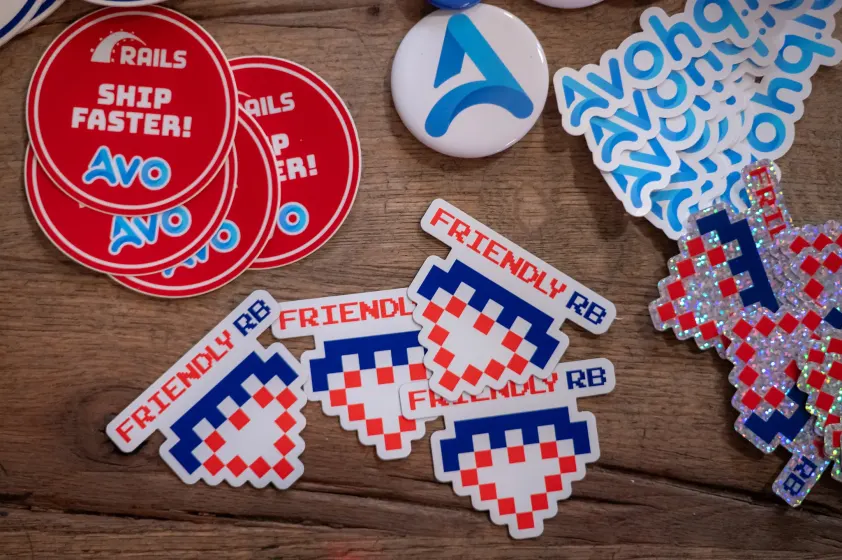Friendly.rb and Avo stickers spread on a wooden table at Friendly.rb 2023